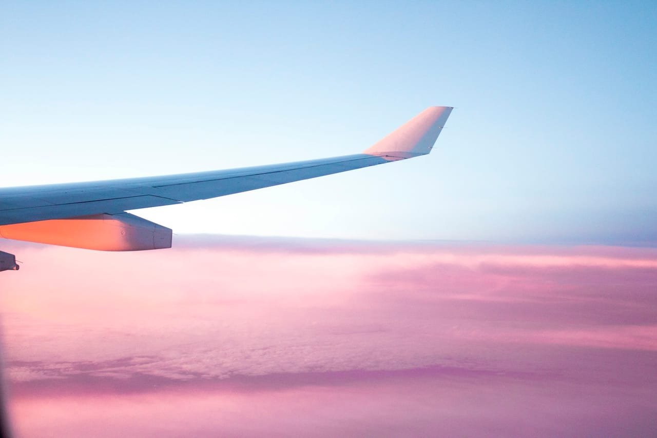 Aircraft wing over pink clouds at dusk